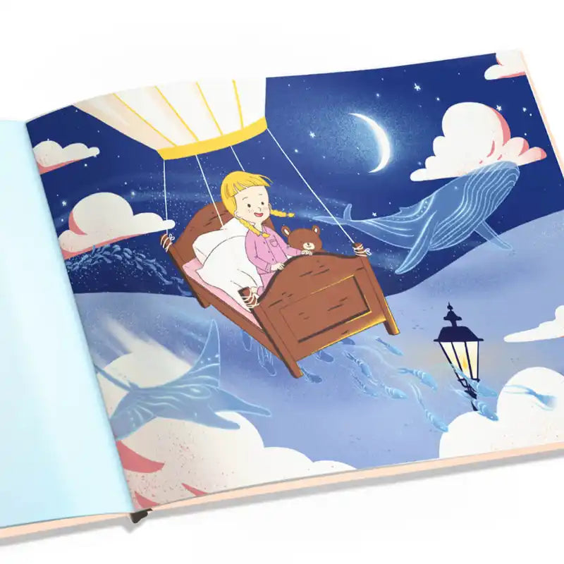 In "Weil du das Größte für mich bist" von Framily zeigt eine zauberhafte Illustration ein Mädchen mit Teddy auf einem von Ballons getragenen Bett, das durch eine sternenklare Nacht mit Mond, Wolken und blauen Walen schwebt.