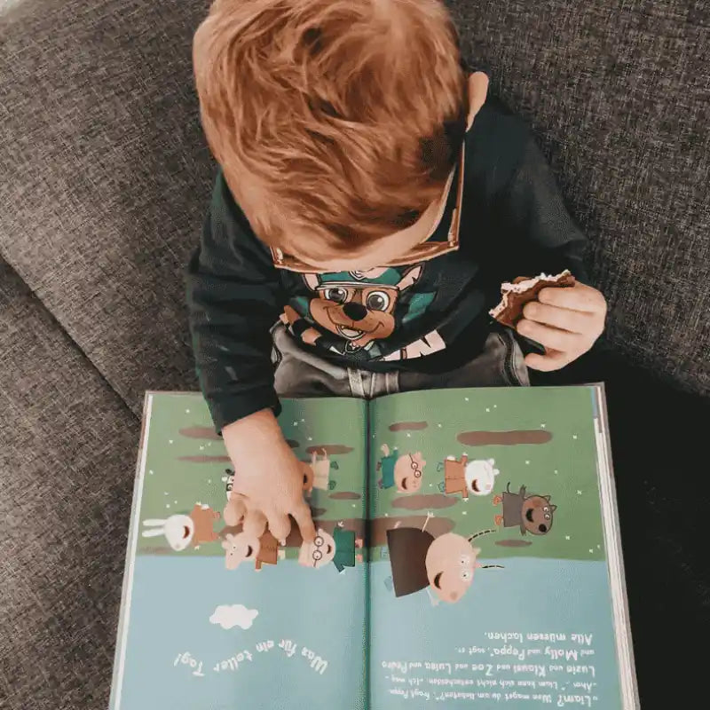 Kind liest ein Peppa-Wutz-Buch mit einem Keks in der Hand.
