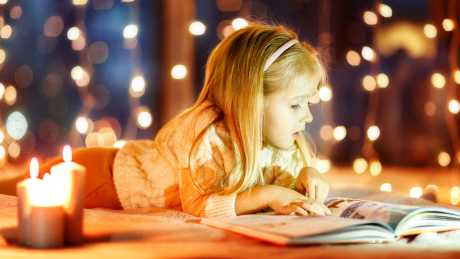 Ein kleines Mädchen liest ein Buch auf dem Boden bei Kerzenlicht
